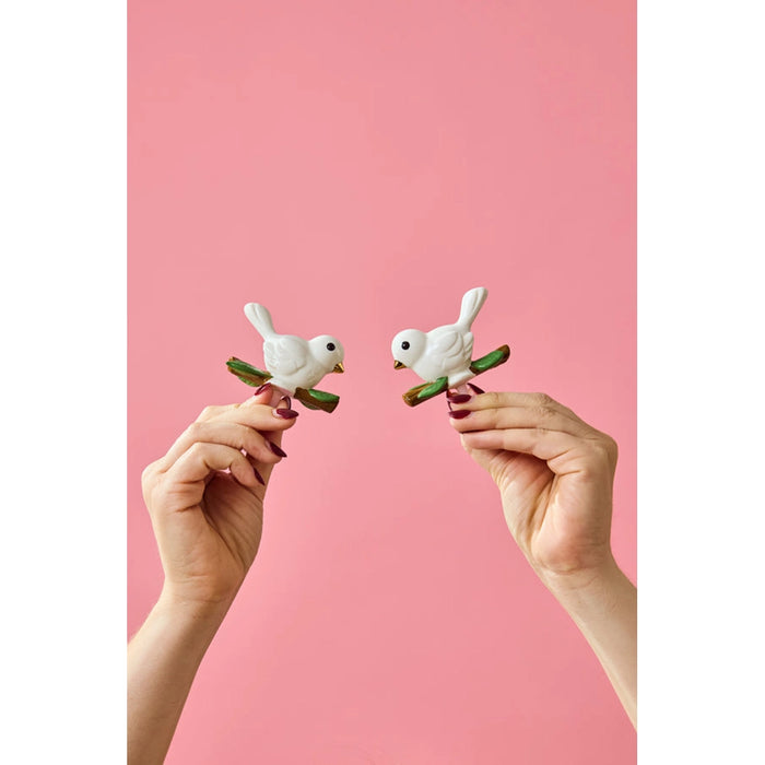 Two hands holding bird-shaped hair clips against a pink background