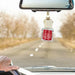A car air freshener bottle labeled 'Apple Bottom Jeans' hanging from a car's rearview mirror while a hand is visible on the steering wheel, with a blurred road and trees in the background.