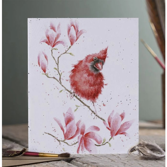 A greeting card depicting a red cardinal perched on a magnolia branch, surrounded by delicate pink flowers.