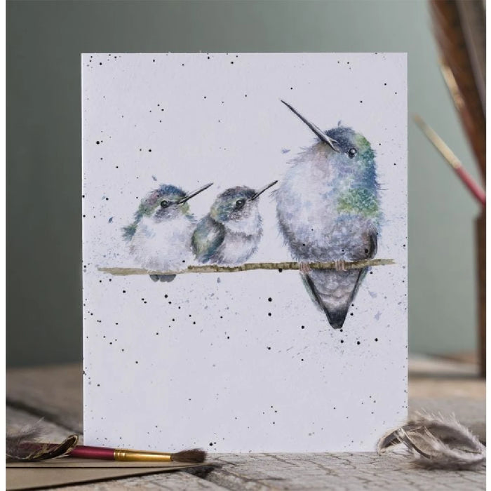 A card featuring three colorful hummingbirds perched on a branch against a soft background.