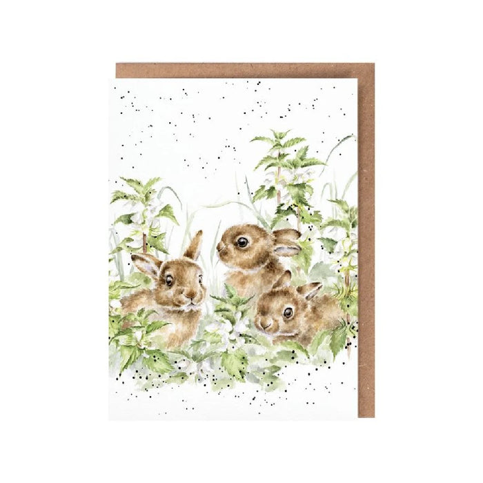 An illustration of three rabbits nestled in vibrant grass on a decorative card.