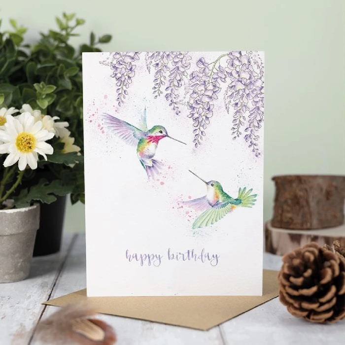 A cheerful birthday card showcasing a hummingbird in flight, adorned with bright floral patterns and celebratory elements.
