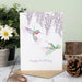 A cheerful birthday card showcasing a hummingbird in flight, adorned with bright floral patterns and celebratory elements.
