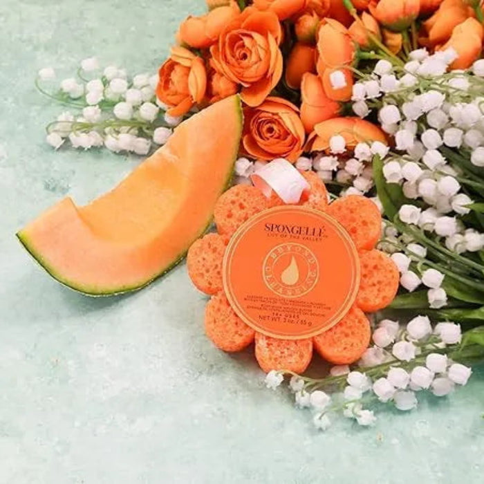 Orange flower-shaped soap with a slice of cantaloupe and flowers on a light green background