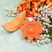 Orange flower-shaped soap with a slice of cantaloupe and flowers on a light green background
