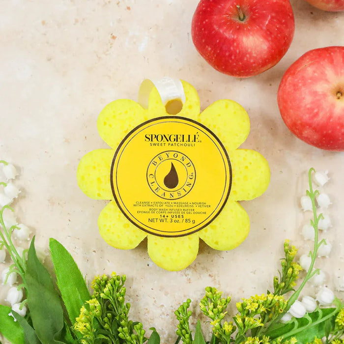 Yellow sponge with 'Spongelle' branding on a textured surface with apples and flowers.