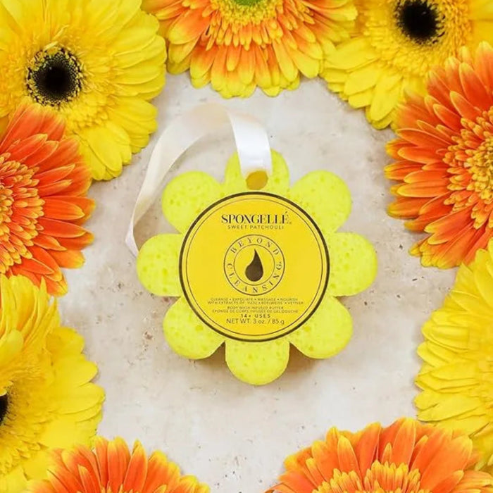 Yellow bath wash  infused buffer with a black droplet design surrounded by orange and yellow gerbera daisies on a light background