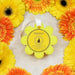 Yellow bath wash  infused buffer with a black droplet design surrounded by orange and yellow gerbera daisies on a light background