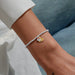 A Littles & Co. Three Generations bracelet worn on wrist with silver beaded band and layered heart charms