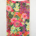 A colorful scarf with a floral pattern hanging on a wall, featuring an array of bright flowers in various shades.