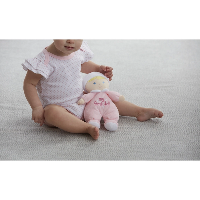 Child holding a pink plush toy with 'my first doll' text on a light gray surface