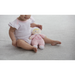 Child holding a pink plush toy with 'my first doll' text on a light gray surface