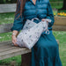 A woman sitting on a bench, holding a bag, appears relaxed in a public park setting.