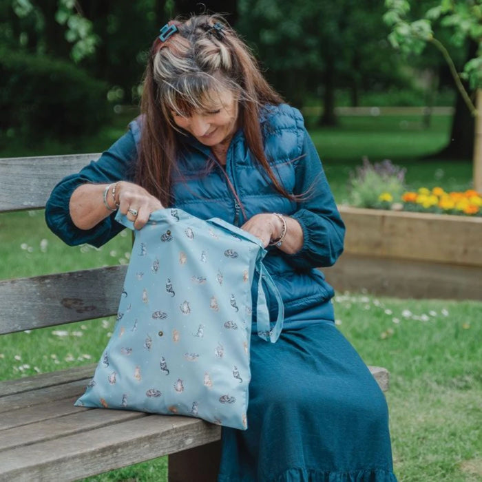 A woman is seated on a bench with a blue bag next to her, appearing calm and contemplative in a public space.