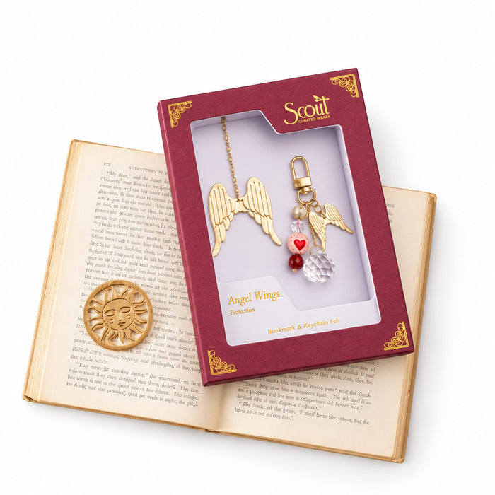 Scout Curated Wears Swallow/Loyalty bookmark and keychain set on a pale pink background. Gold-tone bookmark features a swallow with outstretched wings inside an open circular outline, attached to a long chain with a clear faceted charm