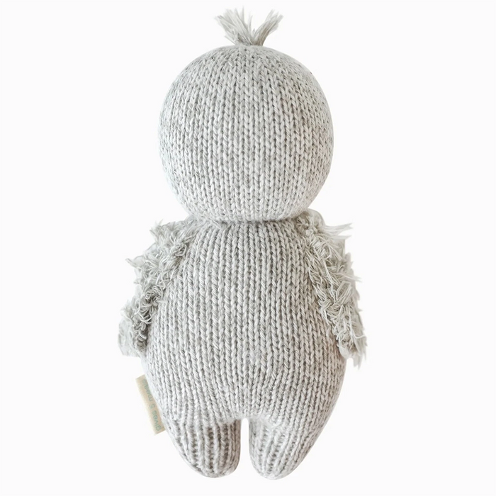 Back view of a hand-knit baby penguin doll in soft gray yarn with fuzzy wings and a little tuft of yarn on its head.