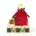 Back view of Snoopy decorating his holiday doghouse with lights, star, and festive patterns.