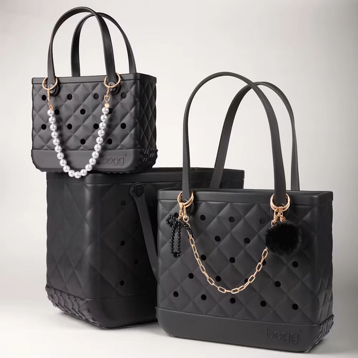 Black faux fur pouf keychain with gold hardware attached to a quilted black Bogg Bag as a stylish bag charm