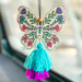 A butterfly air freshener adorned with a colorful tassel, hanging elegantly from its base.