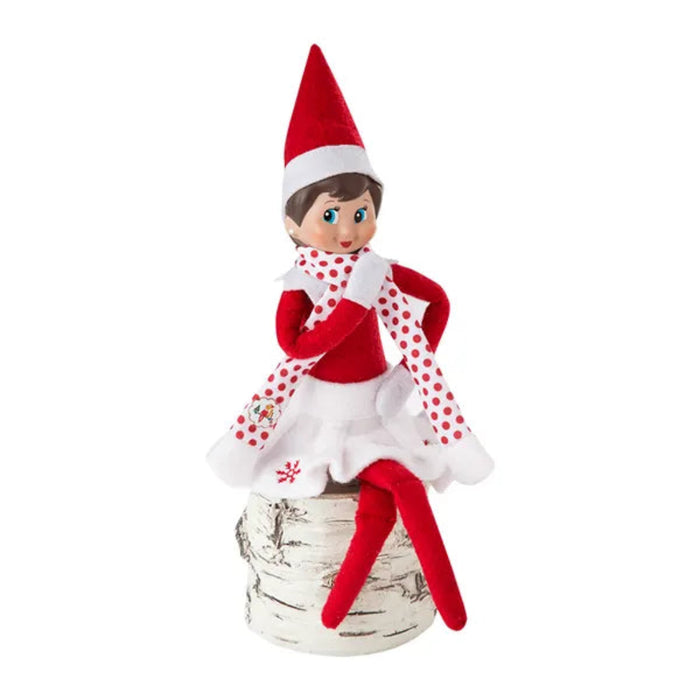 Elf on the Shelf figurine in a red and white outfit with a Santa hat, sitting on a birch log.