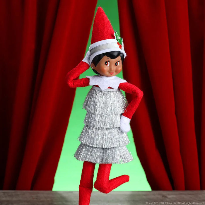 Elf on the Shelf with red hat and dress against a red curtain background