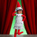 Elf on the Shelf with red hat and dress against a red curtain background