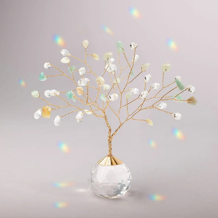 A decorative tree crafted from gold wire and clear and light green beads stands on a faceted crystal ball base. 