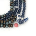 Scout Curated Wears Peace/Dove ceramic bead wrap bracelet/necklace with dark navy, muted green, and bronze-toned round beads, silver-toned spacers, blue-and-white patterned ceramic accents, and a white dove-shaped charm with blue detailing.
