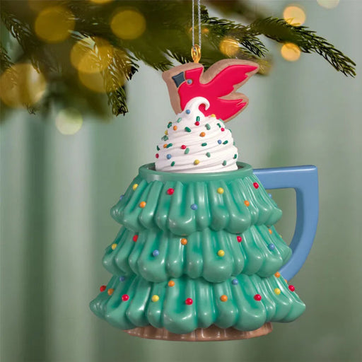 Green tree mug ornament hanging on pine branch with gold loop and cardinal cookie detail