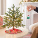 Green tree mug ornament hanging on lit Christmas tree with fireplace background display