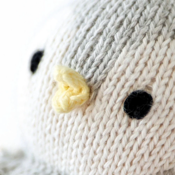 Close-up of the baby penguin doll’s face showing black stitched eyes and a small yellow beak on soft gray and cream knit fabric.
