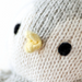 Close-up of the baby penguin doll’s face showing black stitched eyes and a small yellow beak on soft gray and cream knit fabric.