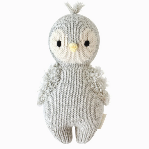 Front view of a hand-knit baby penguin doll in gray and cream yarn with a yellow beak, black stitched eyes, fuzzy wings, and a tuft of yarn on its head.