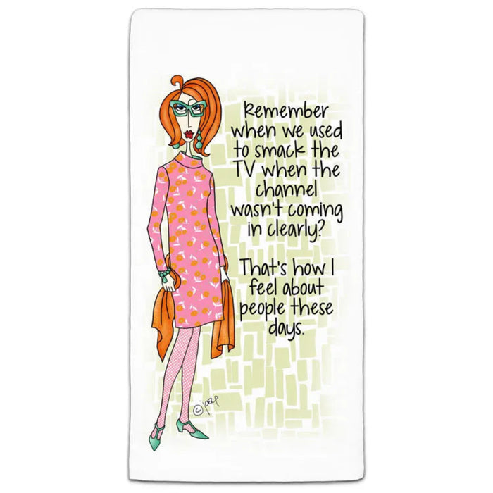 A white rectangular towel featuring a cartoon illustration of Daphne Blake in a pink patterned dress with orange hair, holding an orange bag, next to black handwritten text that reads, 'Remember when we used to smack the TV when the channel wasn't coming in clearly? That's how I feel about people these days.'.
