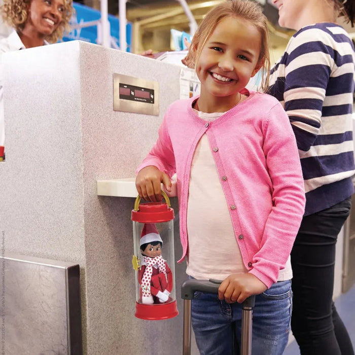 Child holding a red lantern with a doll inside, standing in front of a refrigerator.