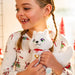 Child holding a white plush toy fox with a heart tag, wearing pajamas with Christmas patterns.