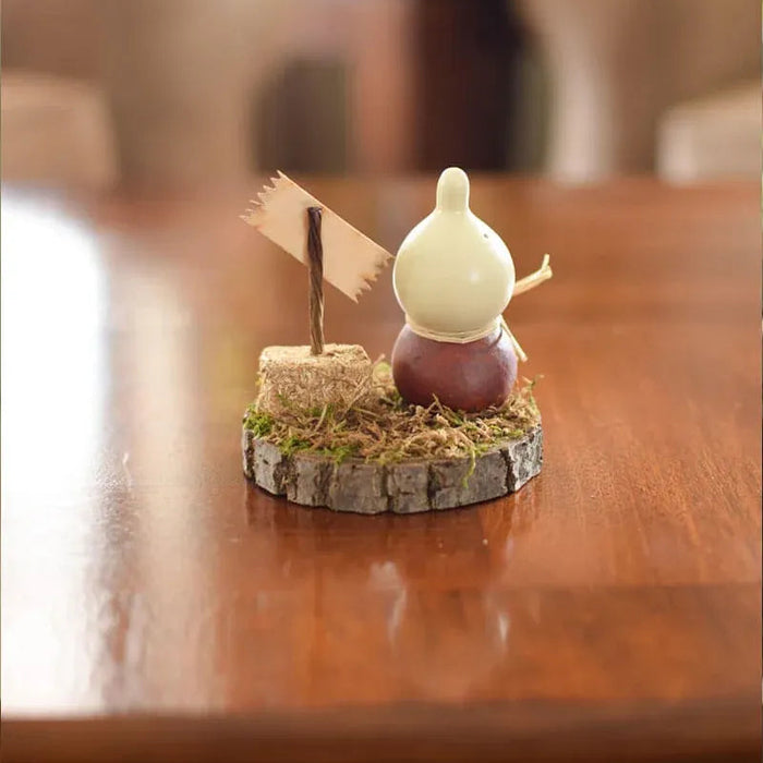 A small decorative tabletop figurine of a white bird perched on a brown round base with a tiny flag and grass, placed on a polished wooden table in a softly blurred indoor setting.