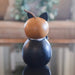 A small decorative gourd figurine shaped like a cat, with a light brown top section, black ears, a dark black lower body, and a thin brown stem, photographed on a reflective surface in an indoor setting.