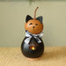 A decorative cat-shaped gourd candle holder with a black body, orange head, black ears, a black-and-white checkered bow, and a small warm light visible through a paw-print cutout, set on a woven surface against a soft beige background.
