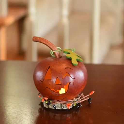 A carved wooden jack-o'-lantern pumpkin decoration with a warm glowing light inside, sitting on a dark wooden table with a softly blurred indoor background.