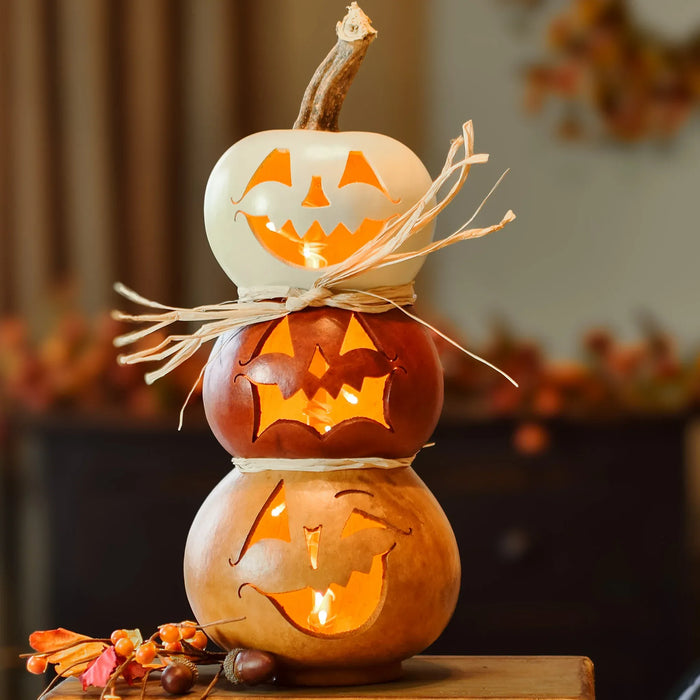 Stack of three carved pumpkins with glowing lights on a wooden surface.