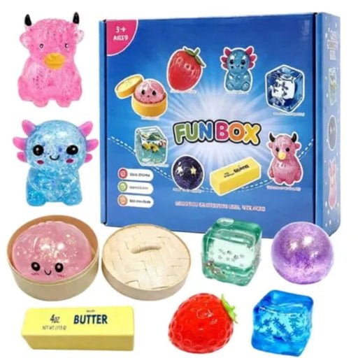 A colorful toy 'FUN BOX' set displayed with its blue retail box and multiple squishy, glittery, and textured toy pieces including a pink horned creature, a blue creature, a strawberry-shaped item, a wooden-texture piece, a translucent green cube, a purple sphere, and a butter block, all arranged on a white background.