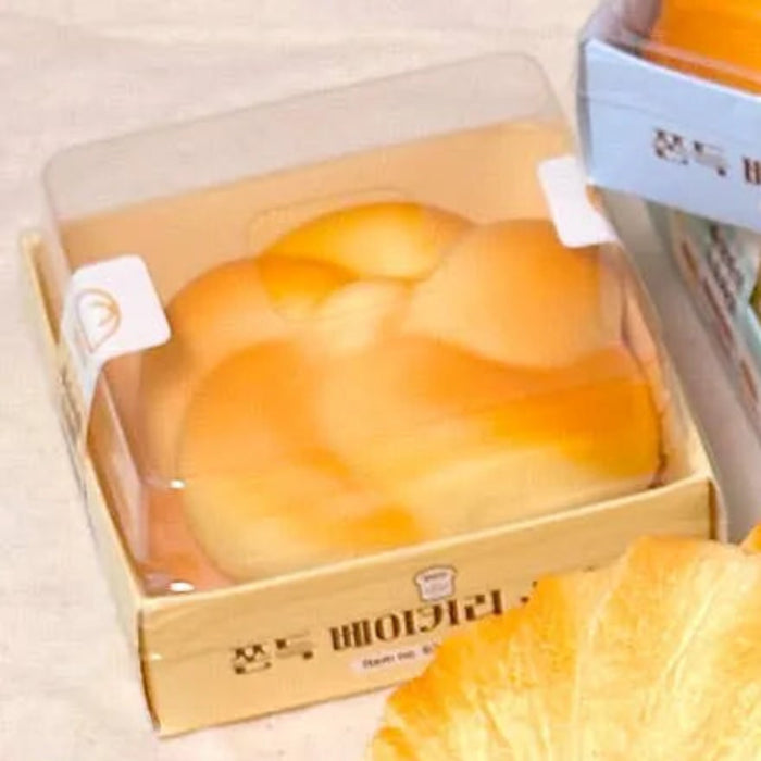 Hand holding a croissant-shaped bread with more bread items and packaging in the background.