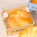 Hand holding a croissant-shaped bread with more bread items and packaging in the background.