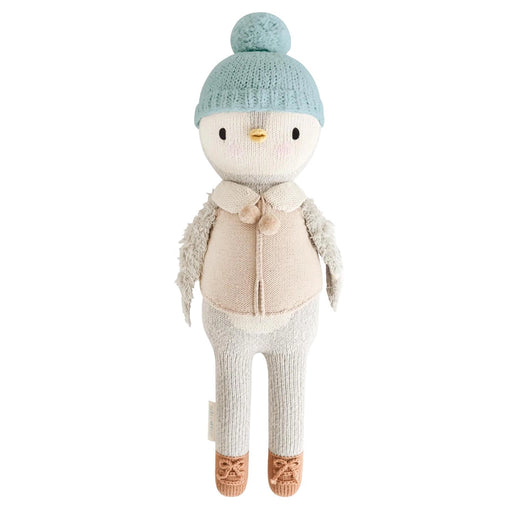 Cuddle + Kind Greyson the Penguin doll wearing a light blue knit hat with pom-pom, beige vest, and brown knit shoes.
