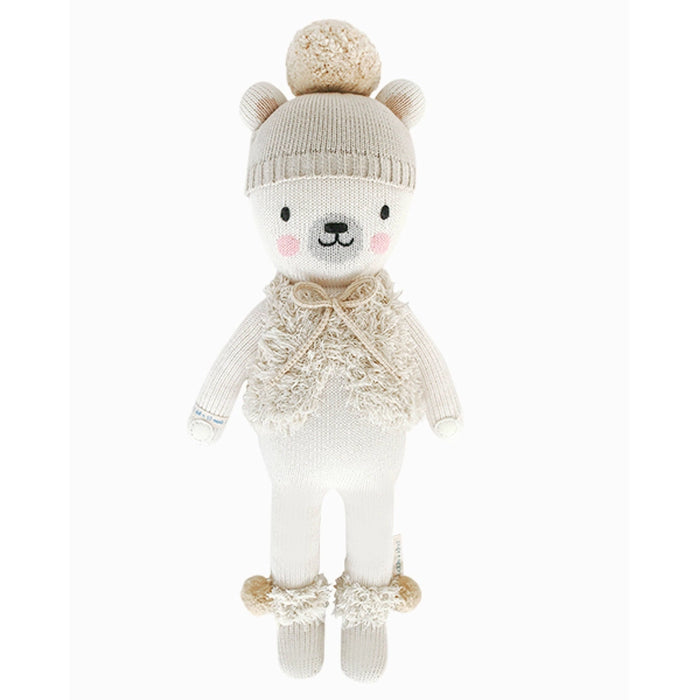 Front view of Stella the Polar Bear doll wearing a knit hat with pom-pom, fuzzy vest, and pom-pom ankle cuffs, smiling with blush cheeks.