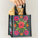 A hand grips a small bag adorned with a vibrant floral pattern, showcasing intricate details.