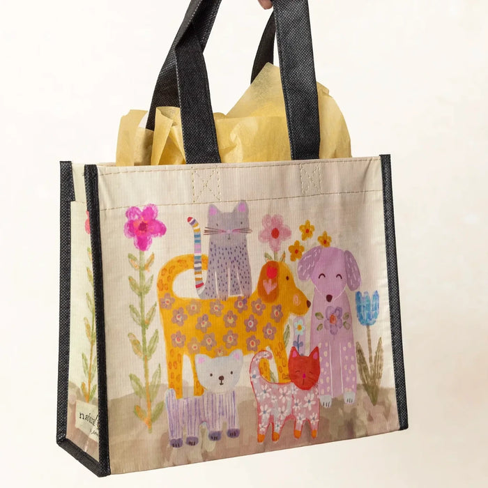 A hand grips a bright bag showcasing various cats and dogs in a playful pattern.