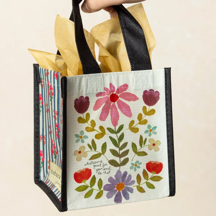 A hand grips a small floral bag, featuring vibrant flowers that add a touch of nature to the accessory.