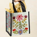 A hand grips a small floral bag, featuring vibrant flowers that add a touch of nature to the accessory.